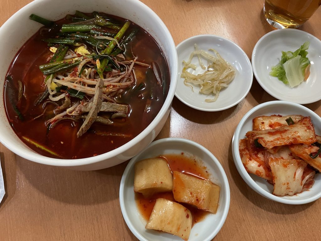 白い大きな器に入ったユッケジャン定食。四角い大根キムチ(カクテキ)と白菜キムチなど、4種類の小皿(パンチャン)が添えられている