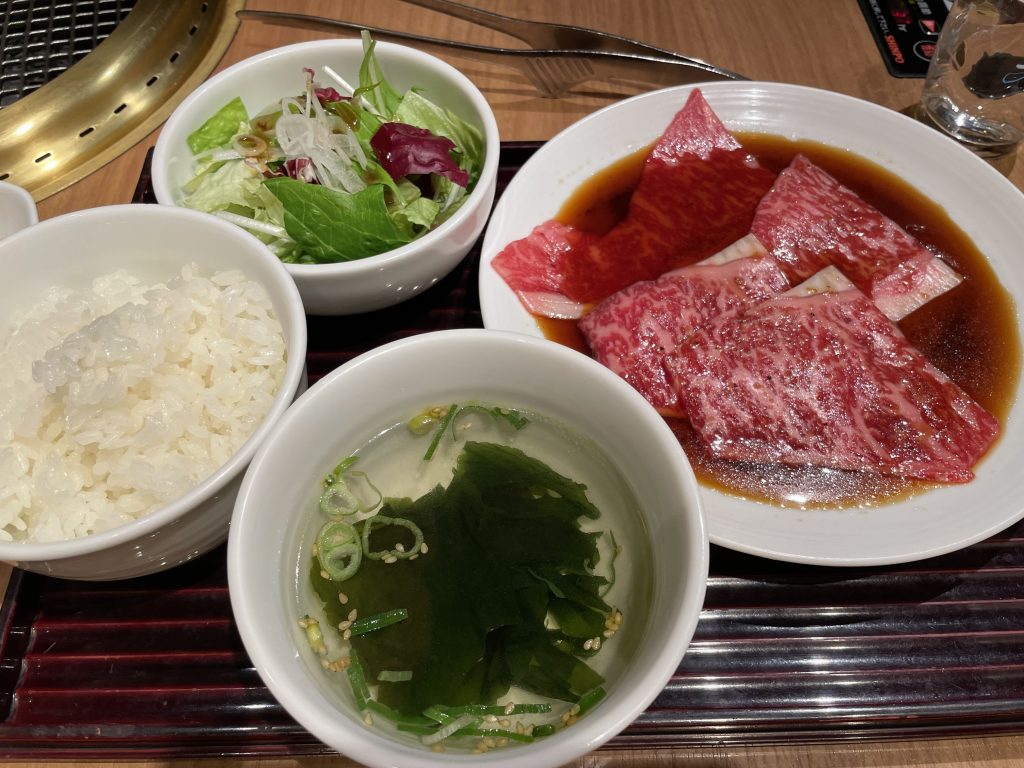 焼肉店で提供される、鮮やかな赤身とサシが入った牛ロース肉のセット。付け合わせにサラダ、スープ、ご飯が添えられている様子