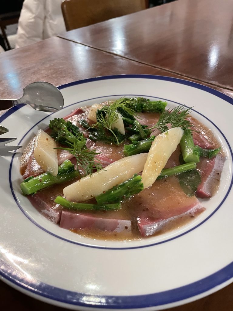 白アスパラガスを添えたカルパッチョ。ディルが飾られ、ソースがたっぷりかかっている。