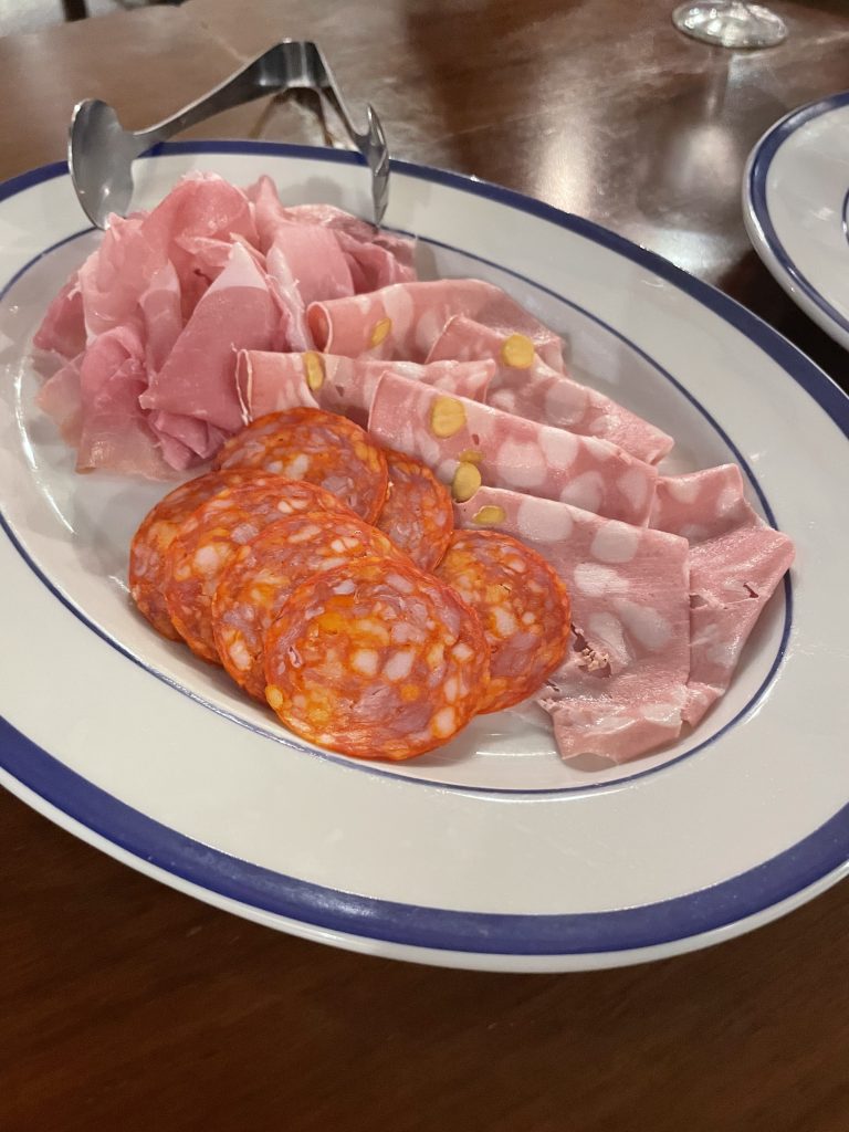 生ハム、サラミ、モルタデッラのハム3種盛り合わせ。青い縁取りの白い皿に並んでいる。