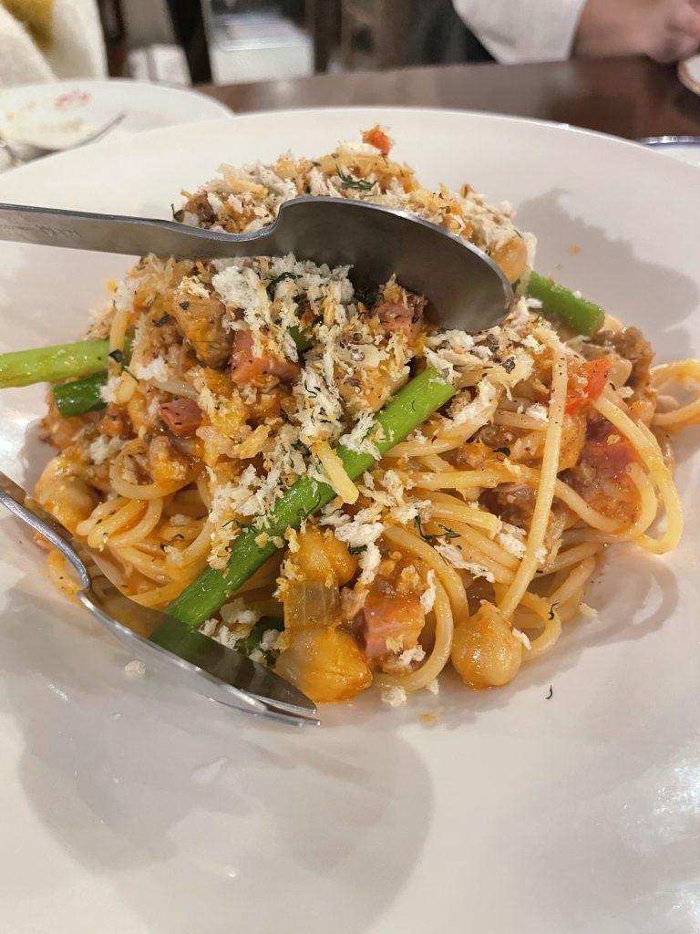 具だくさんのパスタ。アスパラガスやベーコン、ひよこ豆が入り、上からパン粉が散らされている。