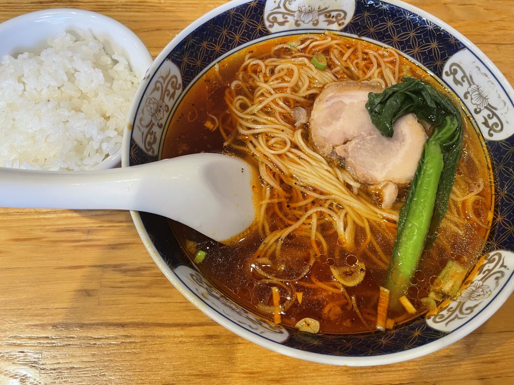 醤油ベースの赤いスープに細麺、チャーシュー、青菜が乗ったラーメンと、横に添えられた白ご飯