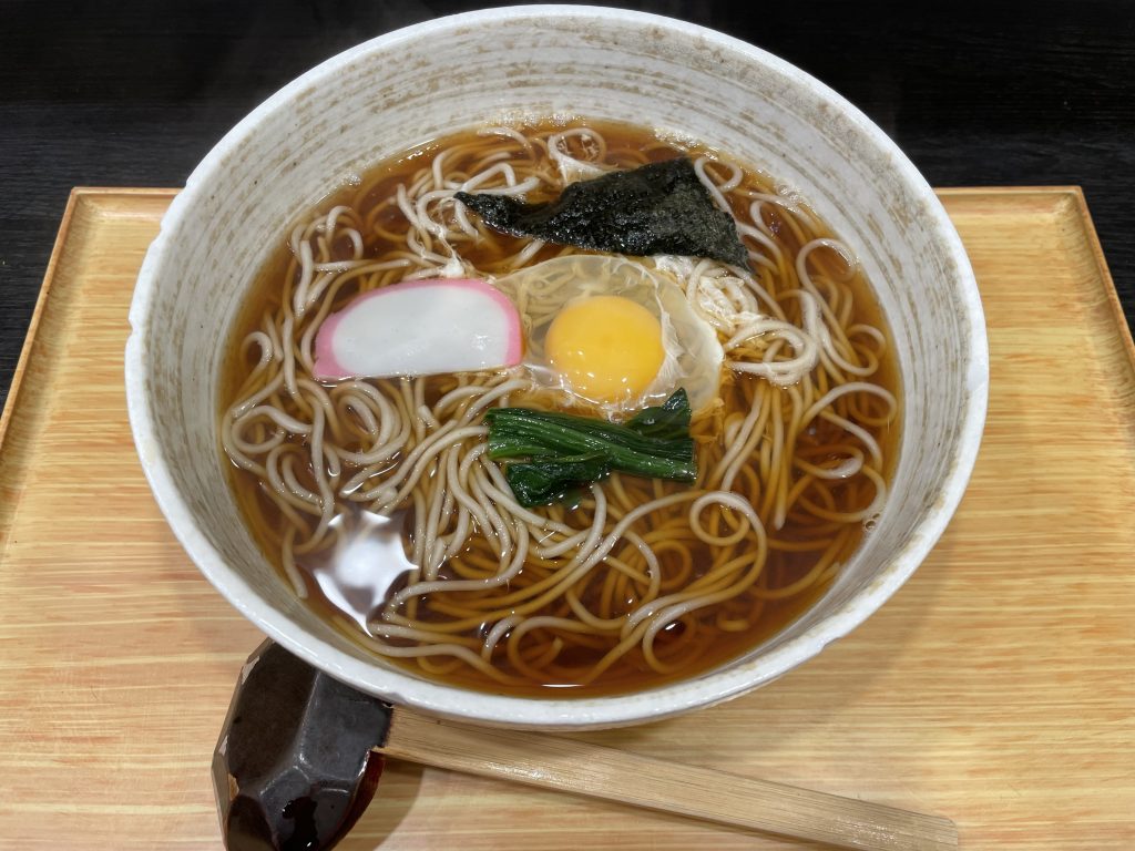 生卵、かまぼこ、ほうれん草、海苔がトッピングされた温かいお蕎麦